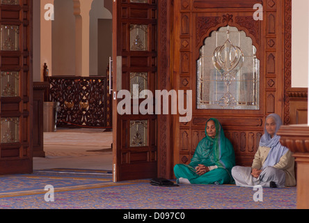 Due anziani asiatici indiano sikh seduto sul pavimento in un Darbar Sahib di un Gurdwara Sikh con le mani in preghiera Foto Stock