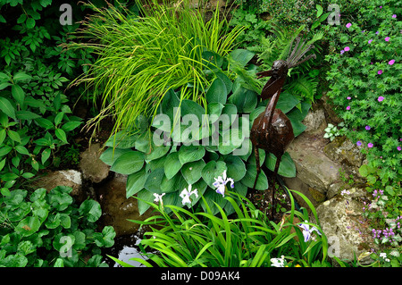 Piacere giardino, un bacino con piante acquatiche, hosta e decorazione con un uccello in metallo. Foto Stock