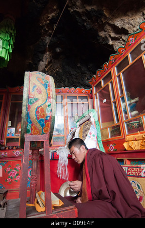 Giovane monaco buddista ring bell come egli mantiene la veglia di preghiera nella cappella costruita in grotta, Sangrgompa Monastero, Namtso Lake, Tibet Foto Stock