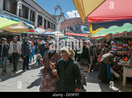 Due pellegrini con ruote della preghiera spingere attraverso affollato mercato all'aperto, Lhasa, in Tibet, in Cina Foto Stock