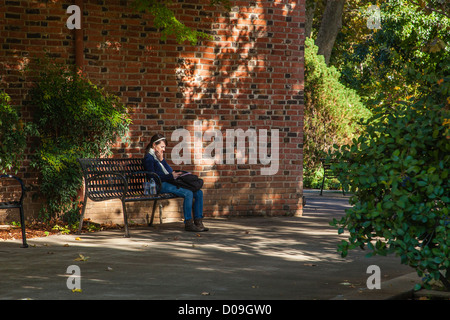 Una femmina di studente di college si rilassa, seduto su un metallo una panchina nel parco del campus della California State University, Chico e i messaggi di testo Foto Stock