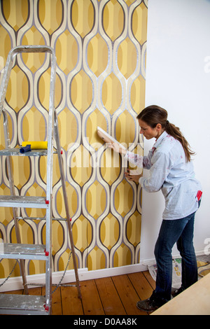 Giovane moglie sta rinnovando la sua casa. Paperhanging, nuovo sfondo. Fai da te. Foto Stock
