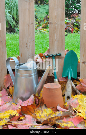 Accessori giardino su foglie di fronte una staccionata in legno in giardino Foto Stock