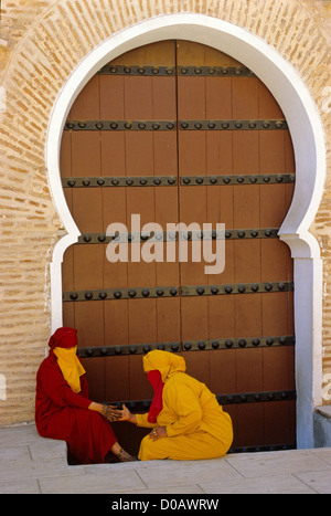 Donne che indossano DJELLABAS e veli Il vestito tradizionale di fronte a un cancello su Djemaa el Fna a Marrakech marocco AFRICA Foto Stock