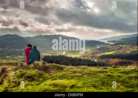 Coppia giovane, maschile si siede sulla roccia, femmina si siede sul suo ginocchio, si affacciano sulla valle, autunno sfondo montagnoso, cielo tempestoso Foto Stock