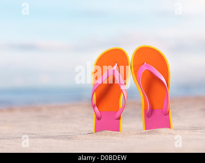 In prossimità di una coppia di colorato arancione flip flop nella sabbia in spiaggia sotto il cielo blu sullo sfondo Foto Stock