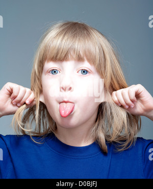 Ragazzo con capelli lunghi biondi fuori la sua linguetta e tirando le orecchie Foto Stock