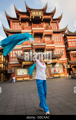 Una donna anziana esegue il cinese la danza della ventola per esercitare nella storica Yu Yuan Gardens Shanghai, Cina Foto Stock