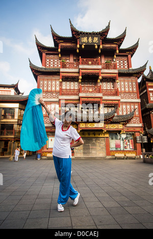 Una donna anziana esegue il cinese la danza della ventola per esercitare nella storica Yu Yuan Gardens Shanghai, Cina Foto Stock