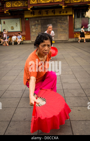 Una donna anziana esegue il cinese la danza della ventola per esercitare nella storica Yu Yuan Gardens Shanghai, Cina Foto Stock