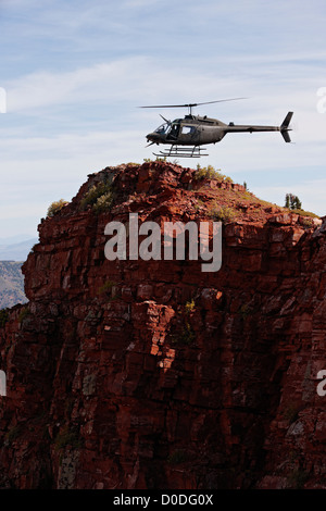 Una campana OH-58 Kiowa aleggia appena al di sopra di una ripida scogliera alta in Colorado di montagne rocciose. Foto Stock