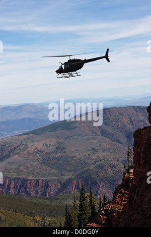 Una campana OH-58 Kiowa aleggia appena al di sopra di una ripida scogliera alta in Colorado di montagne rocciose. Foto Stock