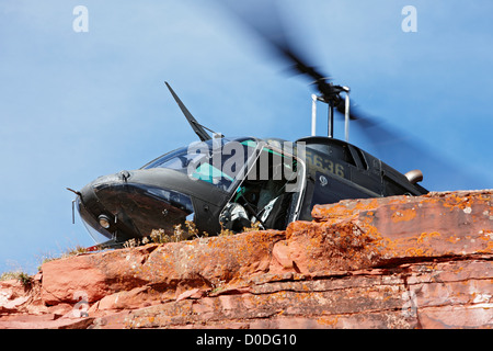 Una campana OH-58 Kiowa vola dietro una ripida scogliera alta in Colorado di montagne rocciose. Foto Stock