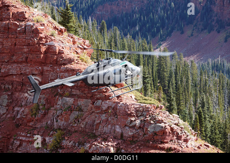 Una campana OH-58 Kiowa aleggia appena al di sopra di una ripida scogliera alta in Colorado di montagne rocciose. Foto Stock