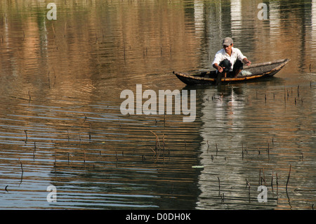 Rete di colata Fisherman da Canoe HUE Vietnam // HUE, Vietnam — Un pescatore getta la sua rete da una canoa di legno nelle acque poco profonde accanto alle canne di Hue, Vietnam. Foto Stock