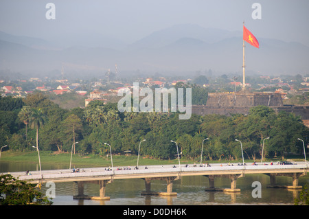 Imperial City Vietnamita Flag Hue Vietnam // HUE, Vietnam — la bandiera vietnamita sulle torri della cittadella della città imperiale sopra la città di Hue, con un ponte sul fiume dei profumi in primo piano. Foto Stock