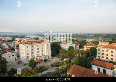 Edifici moderni Hue Vietnam Fiume dei Profumi Montagne | HUE, Vietnam — Edifici moderni, tra cui la filiale della Banca Statale del Vietnam, si ergono sopra il centro di Hue con il Fiume dei Profumi e le montagne nebulose sullo sfondo. Il fiume attraversa il centro geografico della città, separando la citadella imperiale storica sulla riva nord dal quartiere commerciale più recente a sud, una disposizione che risale alla fondazione della capitale da parte della dinastia Nguyễn nel 1802. Foto Stock