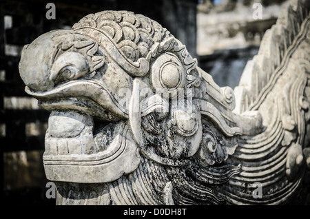 Scultura in pietra della testa di drago della Città Imperiale Hue Vietnam | HUE, Vietnam — Una testa di drago in pietra consumata dal tempo, scolpita con una fronte squamosa e baffi arricciati, protegge una struttura all’interno della Città Imperiale. Le immagini di draghi servivano come emblema supremo dell’autorità della dinastia Nguyễn in questa cittadella, centro politico del Vietnam dal 1802 fino all’abdicazione dell’imperatore Bảo Đại nel 1945, dopo la quale le guerre del 1885, 1947 e 1968 hanno lasciato solo una frazione degli edifici originali in piedi. Foto Stock