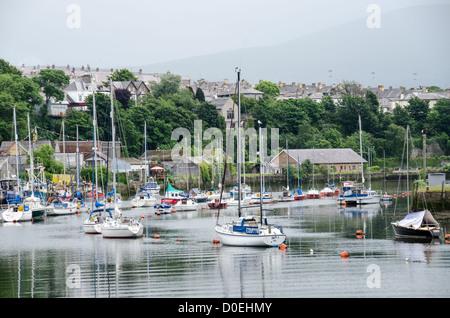 CAERNARFON, Galles - barche a vela ormeggiate in primo piano lungo il fiume Seiont, con la cittadina di Caernarfon visibile sullo sfondo. Il fiume Seiont scorre attraverso questa storica città di mercato nel Gwynedd, Galles nord-occidentale. Caernarfon si trova sulla costa meridionale dello stretto di Menai, che separa la terraferma gallese dall'isola di Anglesey. La città funge da centro amministrativo del Gwynedd ed è ampiamente conosciuta per il suo castello medievale, un sito patrimonio dell'umanità dell'UNESCO. Il fiume Seiont fornisce strutture portuali naturali che hanno sostenuto le attività marittime nella zona per secoli. CA Foto Stock