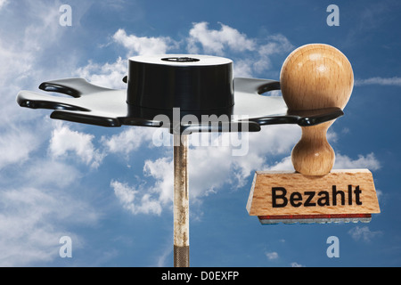 Timbro con iscrizione tedesco Bezahlt (pagato) si blocca in un rack di timbro, sfondo cielo Foto Stock
