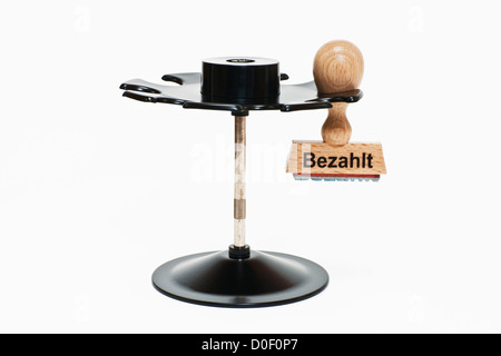 Timbro con iscrizione tedesco Bezahlt (pagato) si blocca in un timbro rack, sfondo bianco Foto Stock