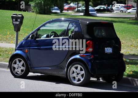 Un'auto Smart molto piccola parcheggiata ad un metro di strada in Ontario, Canada. Tempo limitato. A gettoni. Zona residenziale. Convenzionale. Non elettrico. Foto Stock