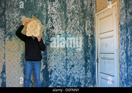 Uomo con carta da parati strappata trinciatrice decadeva in camera blu casa abbandonata interni. Foto Stock