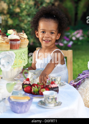 Licenza disponibile a MaximImages.com - ragazza sorridente felice che ha una festa estiva all'aperto. Bere tè con cupcake. Foto Stock