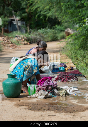 Le donne indiane il bucato a mano su un villaggio rurale road. Andhra Pradesh, India Foto Stock