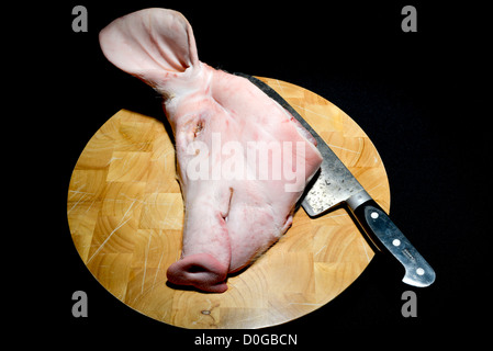Butchered materie suini di testa e una grande cleaver coltello su un legno di faggio macellai di blocco, tagliere con uno sfondo nero. Foto Stock