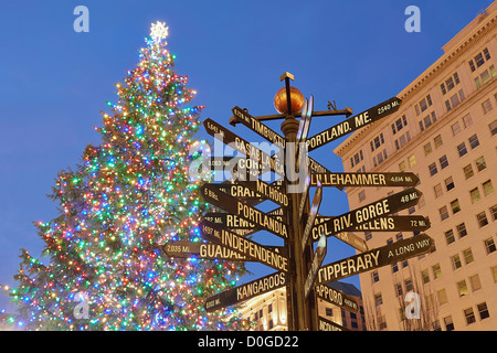 Albero di Natale con luci colorate in Pioneer Courthouse Square con segnaletica direzionale rivolta verso luoghi di tutto il mondo Foto Stock