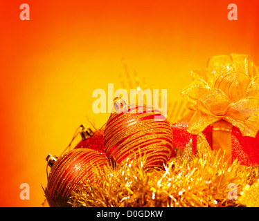Image of Christmas holiday still life isolated on orange background, red decorative baubles, New Year present with golden ribbon Foto Stock