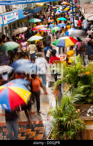 Affollata strada commerciale area in Bridgetown in un giorno di pioggia con persone ombrelli azienda, Barbados, West Indies Foto Stock