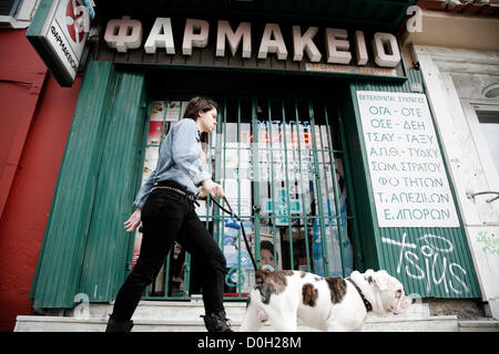 Salonicco, Grecia. Novembre 26, 2012. Una giovane ragazza insieme con il suo cane passeggiate passato una farmacia chiusa. 48 ore di sciopero da farmacie in tutto il paese e si fermano contemporaneamente somministrare farmaci sul credito ai membri dei servizi sanitari nazionali (EOPYY) chi dovrà pagare di tasca propria e la rivendicazione l'importo del fondo. Foto Stock