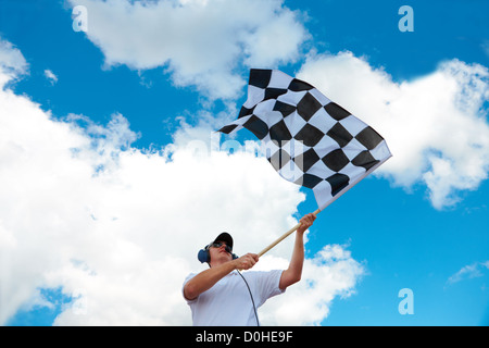 Uomo con cuffie holding e sventola una bandiera a scacchi su una canalina Foto Stock