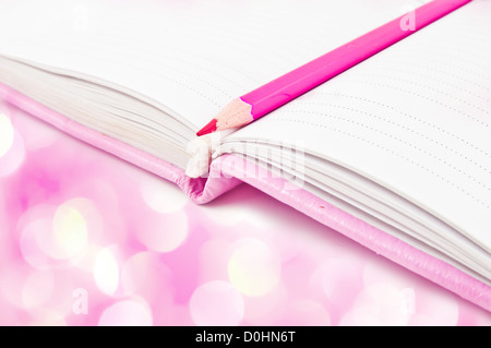 Notebook rosa e matita con luci rosa in background Foto Stock
