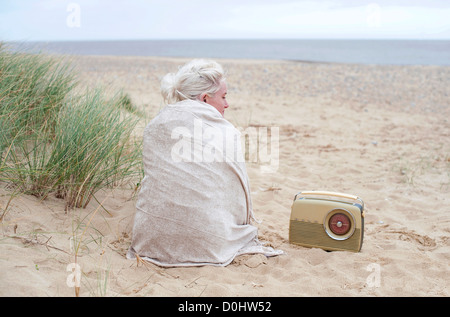 Donna seduta sulla spiaggia avvolti in scialle Foto Stock