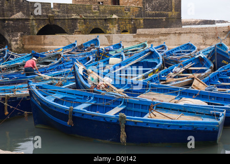 Uomo al lavoro in massa di blu barche da pesca nel porto di Essaouira Foto Stock