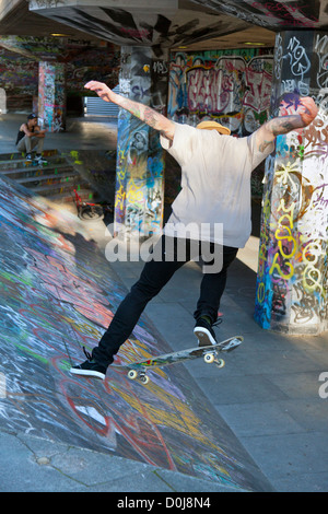 Il salto al guidatore di skateboard graffiti-terra sulla South Bank di Londra. Foto Stock