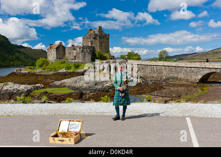 Un lone piper suona di fronte Eilean Donan Castle e Loch Duich. Foto Stock