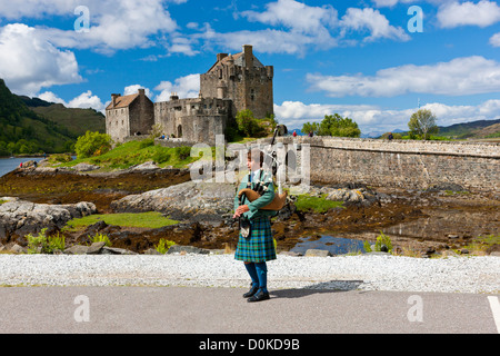 Un lone piper suona di fronte Eilean Donan Castle e Loch Duich. Foto Stock