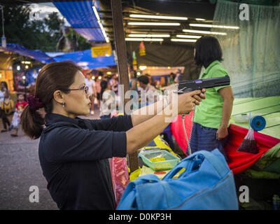 Nov. 27, 2012 - Bangkok, Thailandia - Una donna tailandese prende la mira con una pistola di pellet in una cabina di tiro al Wat Saket Fiera del Tempio a Bangkok. La Thailandia è di fronte a una crescente ondata di violenza pistola ed è alle prese con la procedura per frenare. Nonostante la pistola di rigorose leggi di controllo, più e più pistole stanno mostrando fino in paese. Wat Saket, conosciuto popolarmente come il Golden Mount o ''unità PHU Khao Thong,'' è uno dei più popolari e antichi templi buddisti in Bangkok. ZUMA Press, Inc. / Alamy Live News Foto Stock