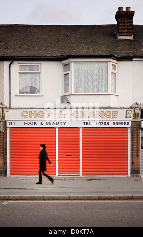 Una donna che cammina passato chiuso un salone di bellezza con persiane rosse in Rainham. Foto Stock