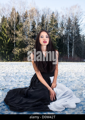 Moda ragazza siede sulla neve in inverno forest Foto Stock