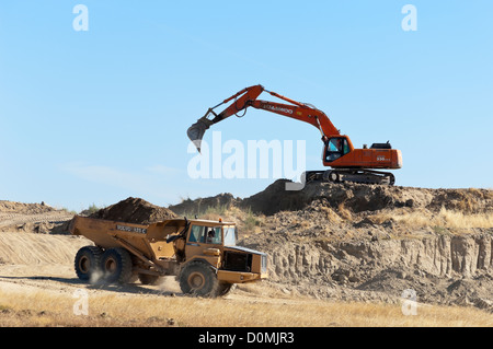 Daewoo escavatore lavora in un cantiere il caricamento di un articolato Volvo dumper Foto Stock