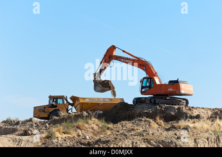 Daewoo escavatore lavora in un cantiere il caricamento di un articolato Volvo dumper Foto Stock