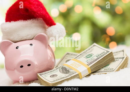 Rosa Salvadanaio indossando Santa Hat vicino a pile di centinaia di dollari di denaro per i fiocchi di neve. Foto Stock