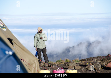 MONTE KILIMANJARO, Tanzania: Un portinaio si erge su un bordo roccioso in cima al monte Kilimanjaro, con nuvole sullo sfondo. Foto Stock