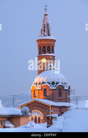 Orientata in verticale immagine della Chiesa cattolica la cupola e la torre campanaria ricoperta di neve in serata in Alba, Italia settentrionale. Foto Stock