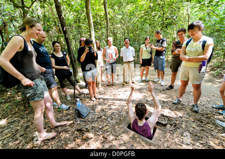 Tunnel di Cu chi Turistico entrando nel tunnel entrata ho chi Minh City Vietnam // CITTÀ DI HO CHI MINH, Vietnam - i turisti tentano di entrare in uno degli ingressi del tunnel preservati nel sito storico di Cu chi Tunnels. L'ingresso mimetico dimostra l'ingegnosità del progetto e della costruzione della rete di tunnel originale. Questi punti di accesso conservati rappresentano parte dell'ampio complesso sotterraneo che si estendeva per oltre 120 chilometri durante la guerra del Vietnam. I tunnel di Cu chi fungevano da rete sotterranea cruciale per le forze vietnamite, fornendo riparo, rotte di rifornimento e vantaggi strategici. Foto Stock